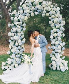 a bride and groom kissing in front of a floral arch with blue hydrangeas