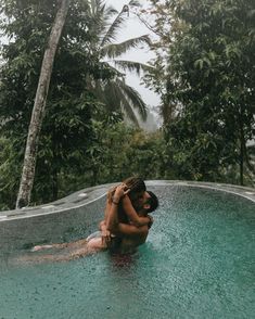 two people are hugging in the middle of an empty swimming pool surrounded by palm trees