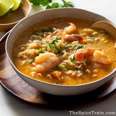 a bowl of shrimp and noodle soup on a wooden plate with lime wedges