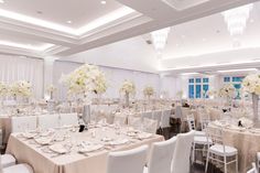 a room filled with lots of tables covered in white linens and centerpieces