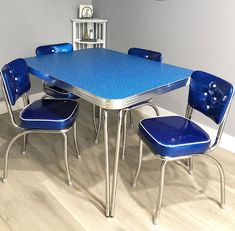 a blue table and chairs in a room with white walls, hardwood flooring and a clock on the wall