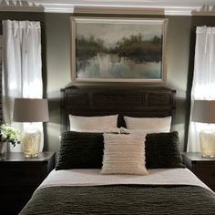 a bed with two lamps on either side of it and a painting above the headboard