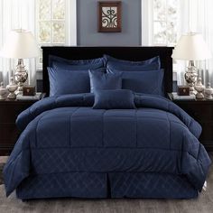 a bed with blue comforter and pillows in a room next to two lamps on a table