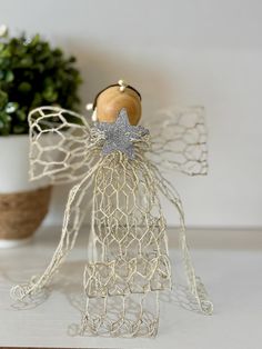 a wire angel sitting on top of a white table next to a potted plant