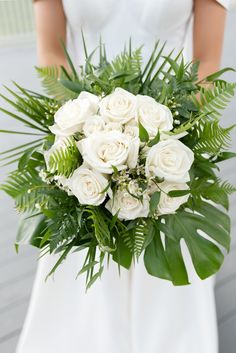 a bride holding a bouquet of white roses and greenery