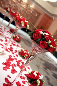 two wine glasses filled with red roses on top of a table covered in white and red petals