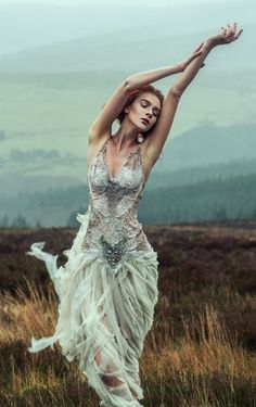 a woman in a white dress is dancing on the grass with her arms stretched out