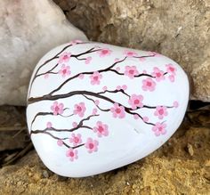 a painted rock sitting on the ground next to a large rock with pink flowers and brown branches