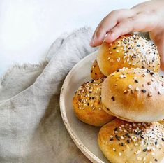 a plate full of sesame seed bagels on top of a white cloth with a hand reaching for one