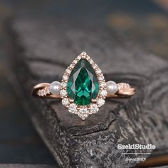 an emerald and white pearl ring on top of a piece of wood with pearls around it