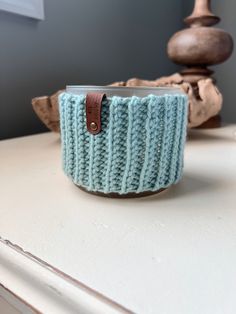 a blue knitted cup holder sitting on top of a white table next to a wooden object