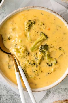 a bowl of broccoli cheese soup with two spoons