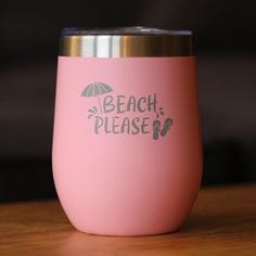 a pink tumbler with the words beach please on it sitting on a wooden table