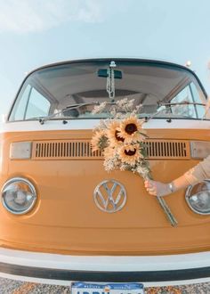 a woman standing next to an old vw bus holding a bouquet of dried flowers