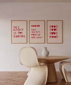 three red and white prints on the wall above a round table with two chairs in front of it