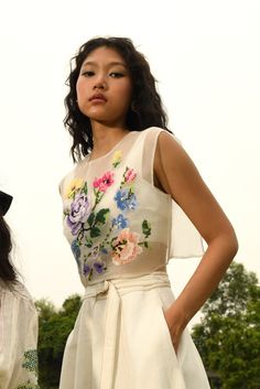 two women standing next to each other wearing dresses with flowers on them and one woman is looking at the camera