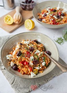 two bowls of pasta with olives, feta cheese and lemon wedges on the side