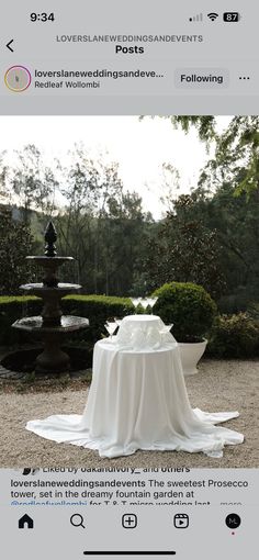 a table with a white cloth on it in the middle of some bushes and trees