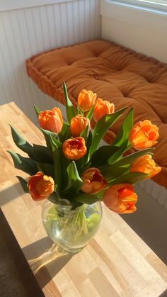 an arrangement of orange tulips in a glass vase on a table next to a bed