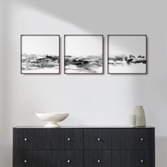 three black and white paintings on the wall above a dresser