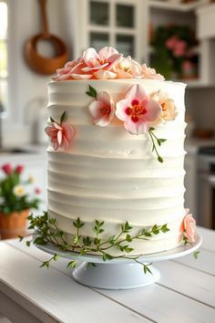 a white cake with pink flowers on it sitting on top of a table in a kitchen