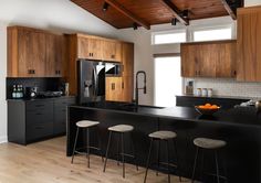 a kitchen with black counter tops and wooden cabinets, along with stools that match the hardwood flooring