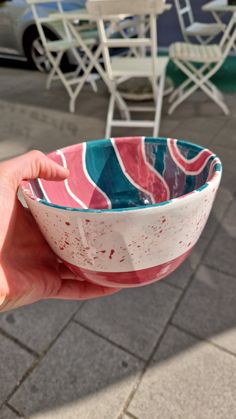 a person holding a bowl in their hand on the sidewalk near some tables and chairs