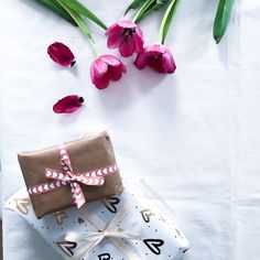 a present wrapped in brown paper with pink tulips on the table next to it