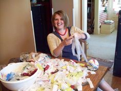 a woman is sitting at a table full of clutter and paper mache pieces