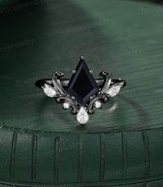 a black diamond ring sitting on top of a green surface with diamonds around it's edges