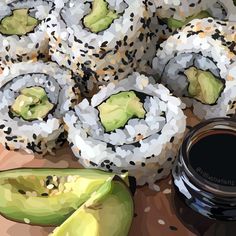 sushi rolls and sliced avocado on a cutting board with a jar of sauce