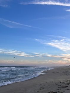 an empty beach with waves coming in to shore and a bird flying over the water