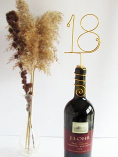 a wine bottle with a gold number on it next to a vase with dried flowers