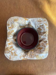 a red bowl sitting on top of a white and gold cloth covered placemat with flowers