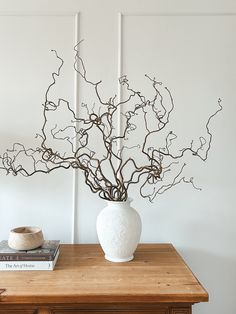 a white vase sitting on top of a wooden table next to a bookshelf