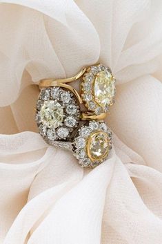 two yellow and white diamond rings sitting on top of a white organe cloth covered tablecloth