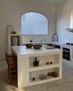 a white kitchen with an island counter and two bowls on the top, in front of a window