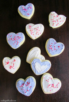 heart shaped cookies with sprinkles are arranged on a wooden table, ready to be eaten