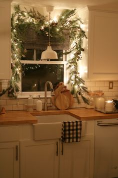 a kitchen decorated for christmas with greenery on the window sill and lights hanging over the sink