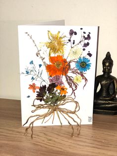 a greeting card with an image of flowers in a vase on a table next to a buddha statue