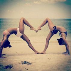 two people doing yoga on the beach making a heart shape