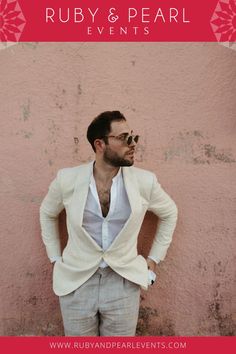 a man standing in front of a pink wall with his hands on his hips wearing sunglasses