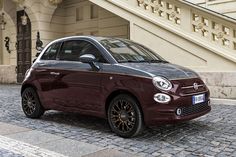 the small car is parked on the cobblestone street