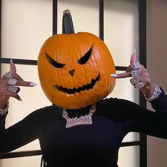 a woman in a black shirt holding two fingers up to her face while wearing a pumpkin mask