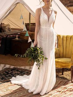 a woman in a white wedding dress holding a green bouquet standing next to a tent