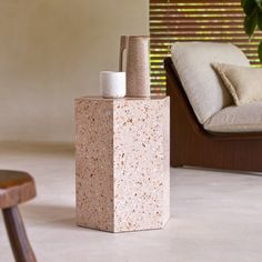 a white vase sitting on top of a cement block next to a chair and pillow