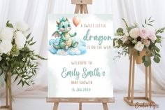 a baby shower sign with a dragon sitting on it's back and balloons in the air