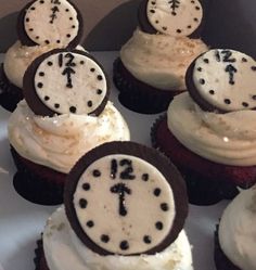 cupcakes with white frosting and black decorations on them are arranged in a box