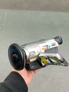 a hand holding a camera with a lens attached to it's body and an object in the foreground