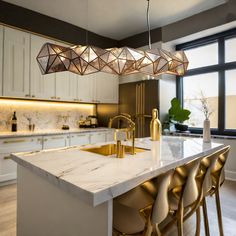 a modern kitchen with marble counter tops and gold accents on the pendant lights over the island